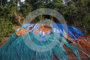 Slope protection with huge plastic sheet to avoid soil erosion when it rains. Colorful pieces of plastic cover lying on