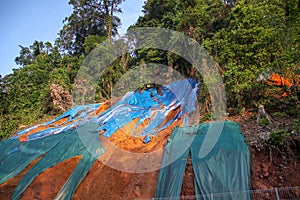 Slope protection with huge plastic sheet to avoid soil erosion when it rains. Colorful pieces of plastic cover lying on