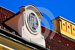 sloped red clay tile residential roof with decorative dormer. oval wood window. yellow stucco ornate chimney.