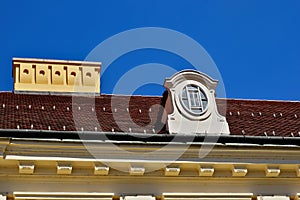 sloped red clay tile residential roof with decorative dormer. oval wood window. yellow stucco ornate chimney.