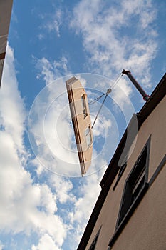 The sloping component for a prefabricated house hovers on the crane rope and hook above a house at a great height