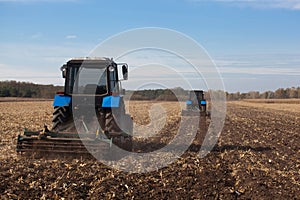 The sloping field. Two large blue traktor plow plowed land after harvesting the maize crop photo