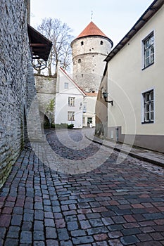 Sloping street of old town behind fortress wall with tower on background