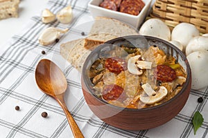 Slovak Christmas national cabbage soup in small black pot with sausage on the tablecloth background