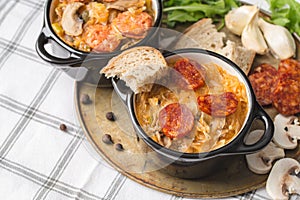 Slovak Christmas national cabbage soup in small black pot with sausage on the tablecloth background