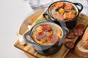 Slovak Christmas national cabbage soup in small black pot with sausage on the tablecloth background