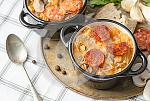 Slovak Christmas national cabbage soup in small black pot with sausage on the tablecloth background