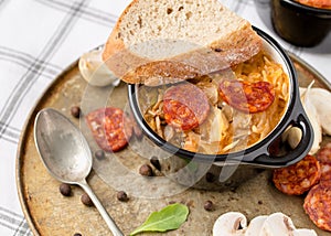 Slovak Christmas national cabbage soup in small black pot with sausage on the tablecloth background