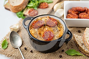 Slovak Christmas national cabbage soup in two small black pots with sausage on the jute background