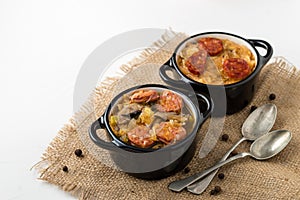 Slovak Christmas national cabbage soup in two small black pots with sausage on the jute background