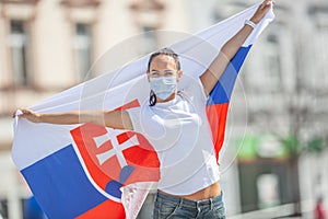 Slovak female fan holds a flag behind her on a street, wearing a face mask