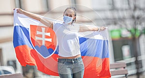 Slovak female fan holds a flag behind her on a street, wearing a face mask