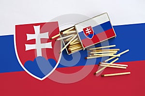 Slovakia flag is shown on an open matchbox, from which several matches fall and lies on a large flag