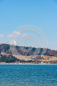 Slovensko: Malá dedinka v blízkosti Tatier. V popredí jazero Liptovská Mara. Zima a snehová hora.