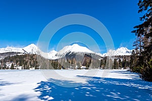 Slovensko, Štrbské Pleso: Pohľad na zamrznuté jazero vo Veľkých Tatrách. Hory v pozadí, stromy a jazero v popredí. Wi