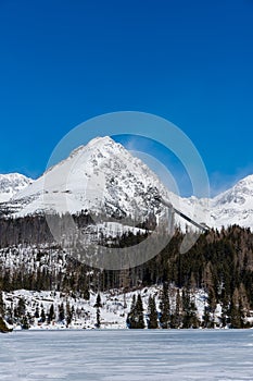 Slovensko, Štrbské Pleso: Pohľad na zamrznuté jazero vo Veľkých Tatrách. Hory v pozadí, stromy a jazero v popredí. Wi