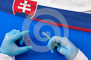 Hands of doctor holding syringe and coronavirus COVID-19 vial vaccine on flag Slovakia