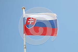 Slovenská vlajka na podložke vo vetre a modrej oblohe