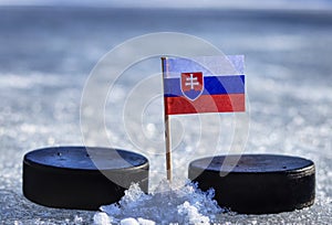 Slovenská vlajka na párátku mezi dvěma hokejovými puky na ledě venku. Slovensko hostí mistrovství světa a Slovensko hraje ve skupině