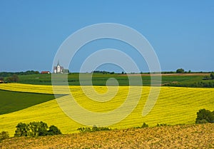 Slovenian countryside in spring with charming little church on a hill and flowering rapeseed field, in Slovenia
