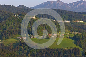 Slovenian countryside in spring with charming little village and small white church on a hill, surrounded by Julian Alps mountains