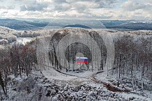 Slovenian flag visible on the top of Ostri Vrh close to grosuplje. Snow panorama, hills and trees are covered with fresh snow