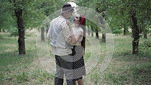 Slow dance of happy elegant young couple in summer park. Smiling loving man and woman dancing outdoors and talking