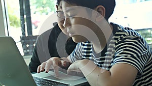 Slow motion 4K Happy asian boy playing game online on laptop computer together . Boy and friend confer with strategy having fun.