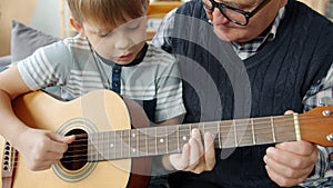 Slow motion of adorable child learning to play the guitar with grandad at home