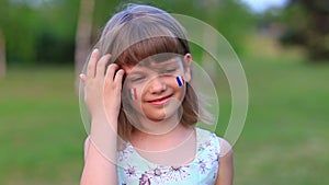 Slow motion of adorable little girl smile at camera with cheeks painted in flag of France. Bastille day on July 14. The
