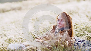 Slow motion. An adult woman in a coat lay down on a picnic mat in a clearing of feather grass that glitters in the rays