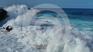 Slow motion aerial shot of ocean wave breaks on the coastal rocks forming white foam and splashes. Flying over atlantic