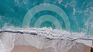 Slow motion aerial video of a beautiful empty beach. Waves break on the sandy shore. Beautiful transparent turquoise sea