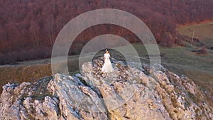 Slow motion aerial view of bride in white wedding dress standing on a cliff