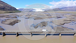 Slow motion aerial view of car crossing a bridge over a glacial river Iceland