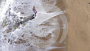 Slow motion aerial view of gorgeous blonde woman walking on remote beach with splashing sea waves