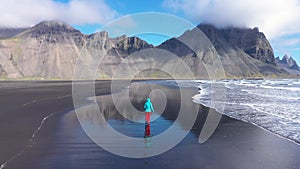 Slow motion aerial view of woman jogging on Atlantic ocean coast. Stokssnes, Vestrahorn mountains, Hofn, Iceland