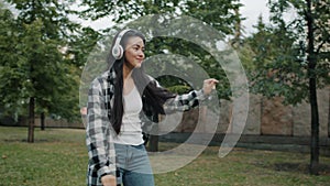 Slow motion of Asian lady dancing outdoors in city park wearing headphones
