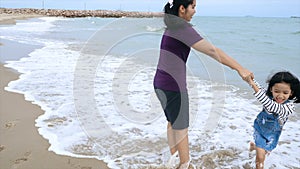 Slow-motion Asian little girl playing with mother on the beach with nature sea wave coast for summer vacation concept
