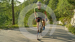 SLOW MOTION: Athletic Caucasian man pedalling his road bicycle up a steep hill.