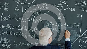 Slow motion back view of senior man writing calculations and formulas on chalkboard