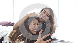 Slow motion - Beautiful young asian women LGBT lesbian happy couple sitting on bed hug and using phone taking selfie together.