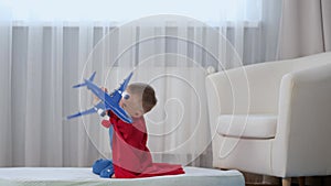 Slow motion blond caucasian boy super hero kid playing with toy air plane, jumping on mattress, trampoline with toy in