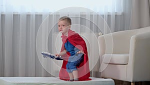 Slow motion blond caucasian boy super hero kid playing with toy air plane, jumping on mattress, trampoline with toy in