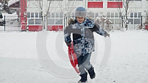 Slow motion of boy happily running with plastic sleds in the snow, enjoying the fresh air and winter scenery.