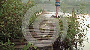 slow motion of a boy running on a wooden pier and jumping into the lake.