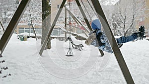 Slow motion of boy swinging in a playground during a winter snowfall. Concept of winter fun, outdoor activities.