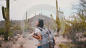 Slow motion camera follows young happy tourist woman with backpack exploring big Saguaro cactus desert at national park.