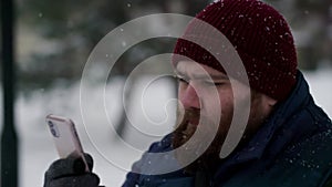 Slow motion a casual young guy using telephone in winter when snowing. Snow falling when man scrolling news in