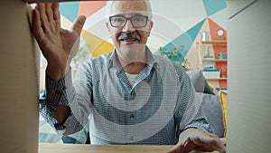Slow motion of cheerful old man in glasses opening carton box smiling looking inside